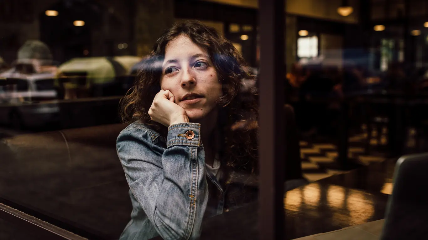 A person looking thoughtfully out of a café window — the wait between conversion submission and approval